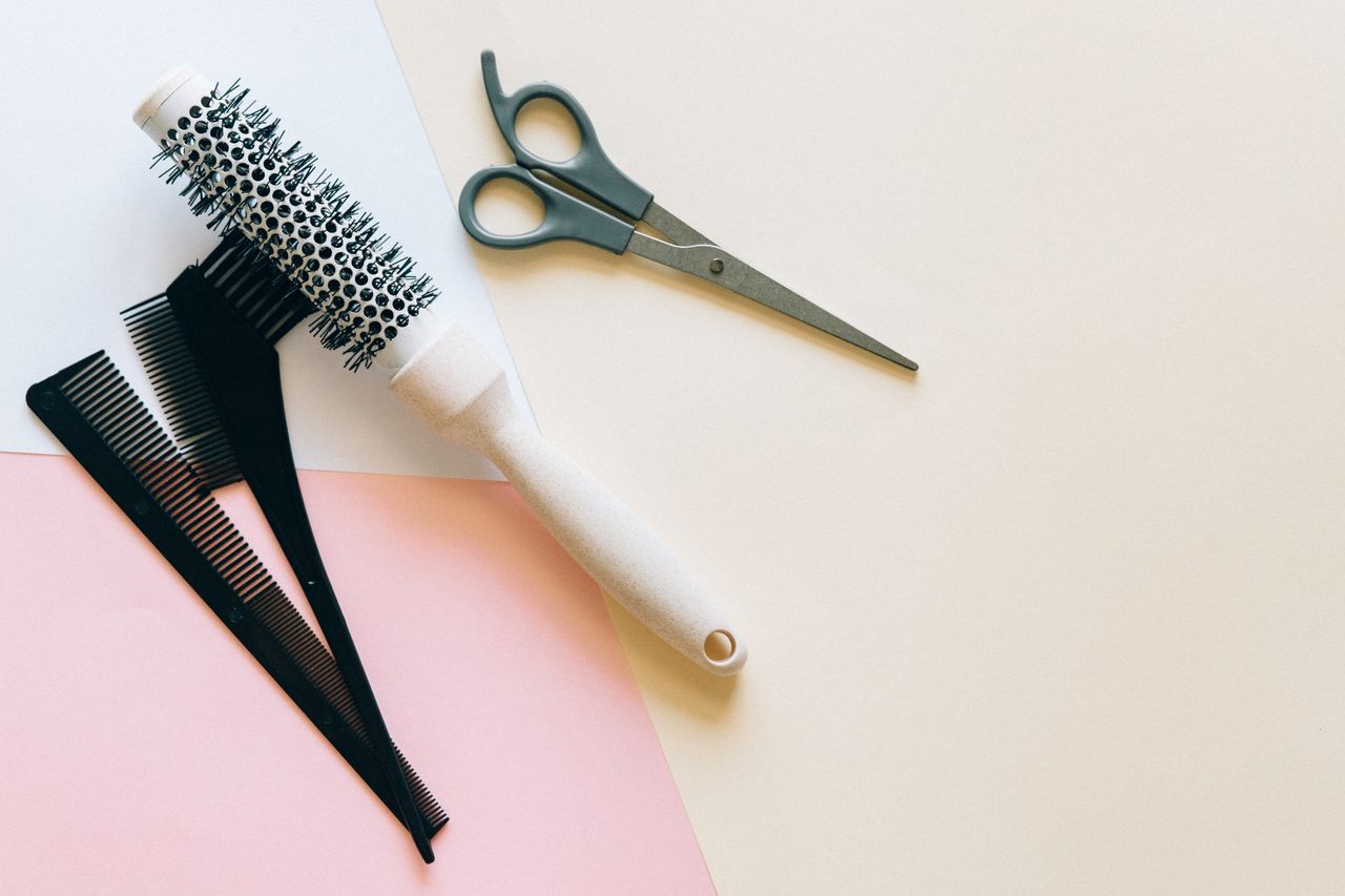 A top view of scissors, combs, and a brush for hairdressing on a pastel surface.