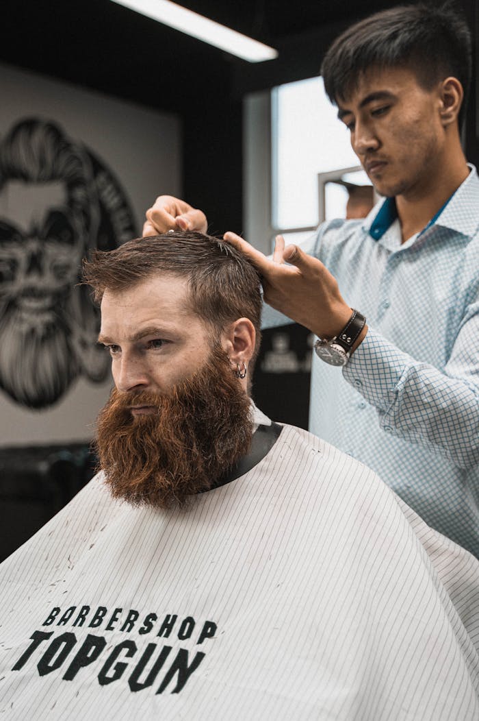 A man with a beard getting a haircut at a modern barber shop by a hairstylist.